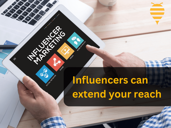this graphic features an ipad with an infographic on it featuring the components of influencer marketing. The man is pointing to a particular function of influencer marketing, that being word of mouth. There is overlay text highlighting that influencers can extend your business' reach. In the top right is the swarm digital marketing logo.